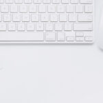 Photo of white keyboard, mouse, plant, coffee cup and notebook