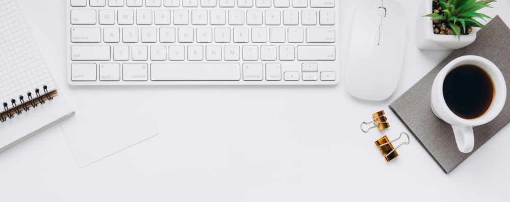 Photo of white keyboard, mouse, plant, coffee cup and notebook